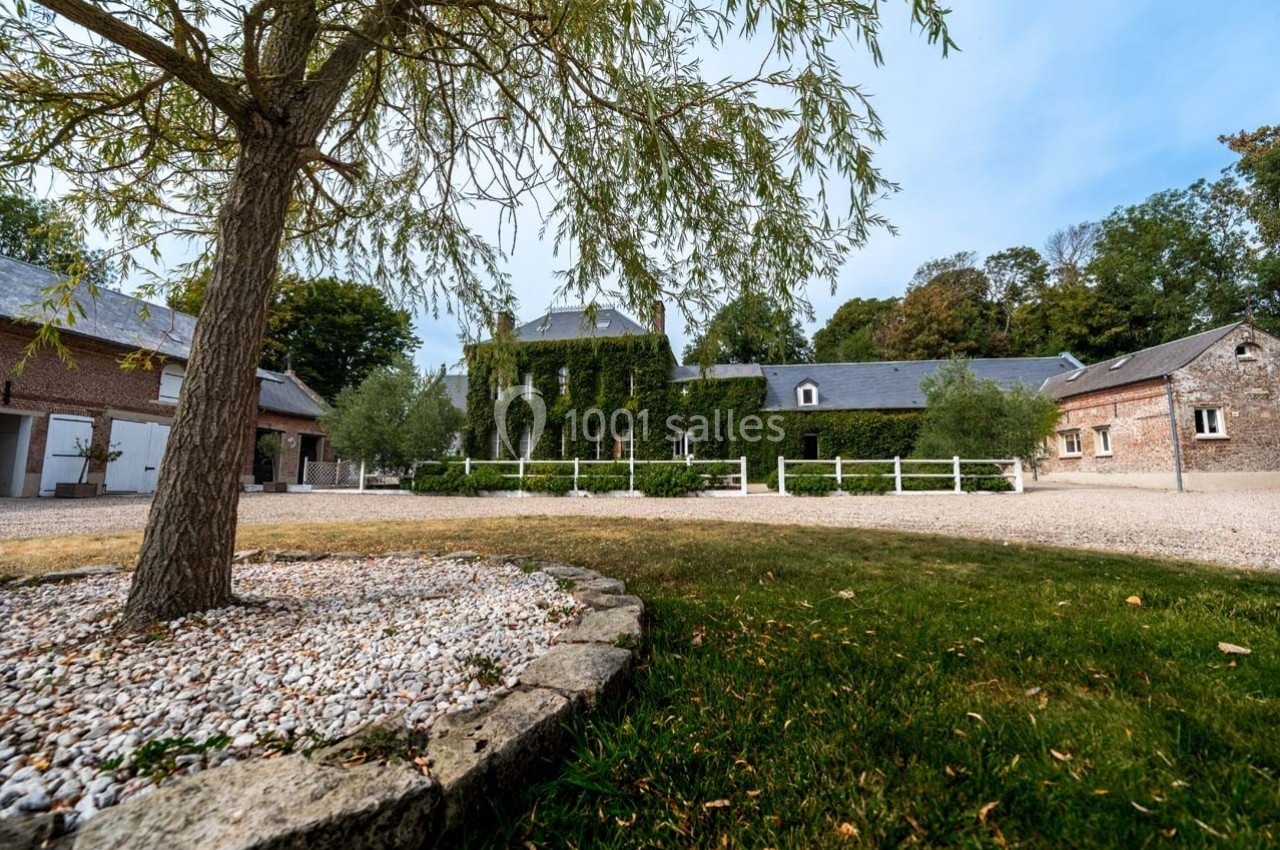 Cour d'une propriété avec bâtiments en briques et en pierre, façade principale couverte de lierre, arbre au premier plan.