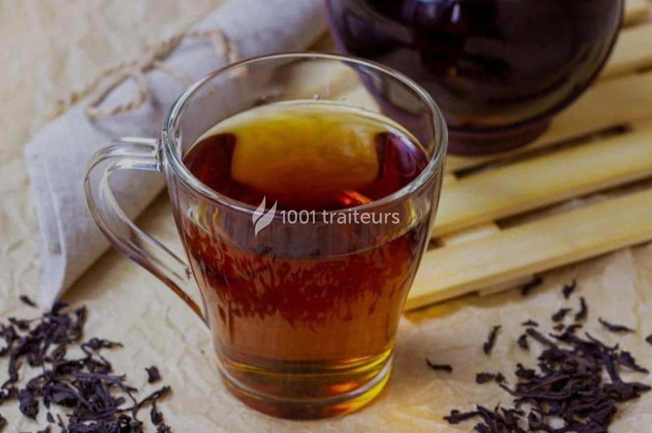 Tasse de thé noir chaud sur une table avec des feuilles de thé séchées et un tissu enroulé à proximité.
