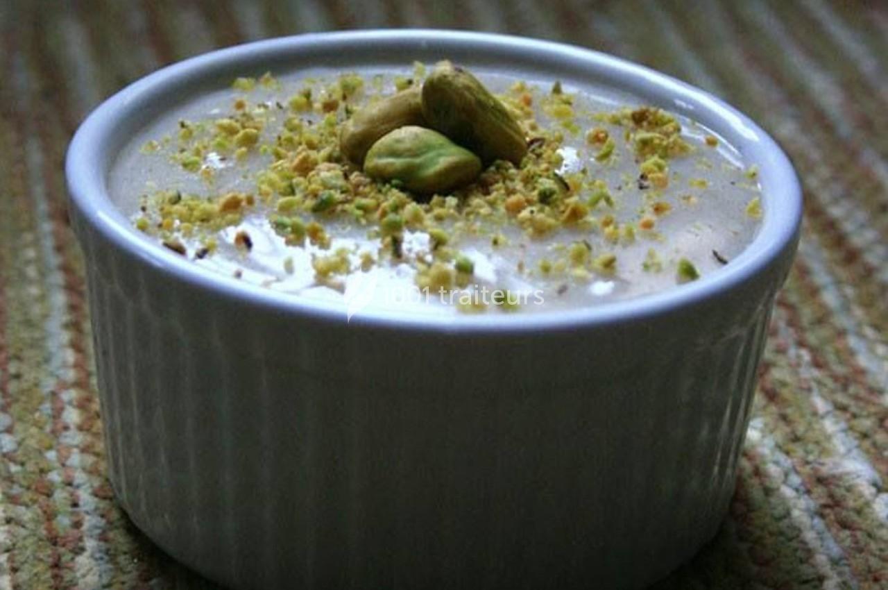 Dessert crémeux dans un ramequin blanc, garni de pistaches concassées et entières sur le dessus.