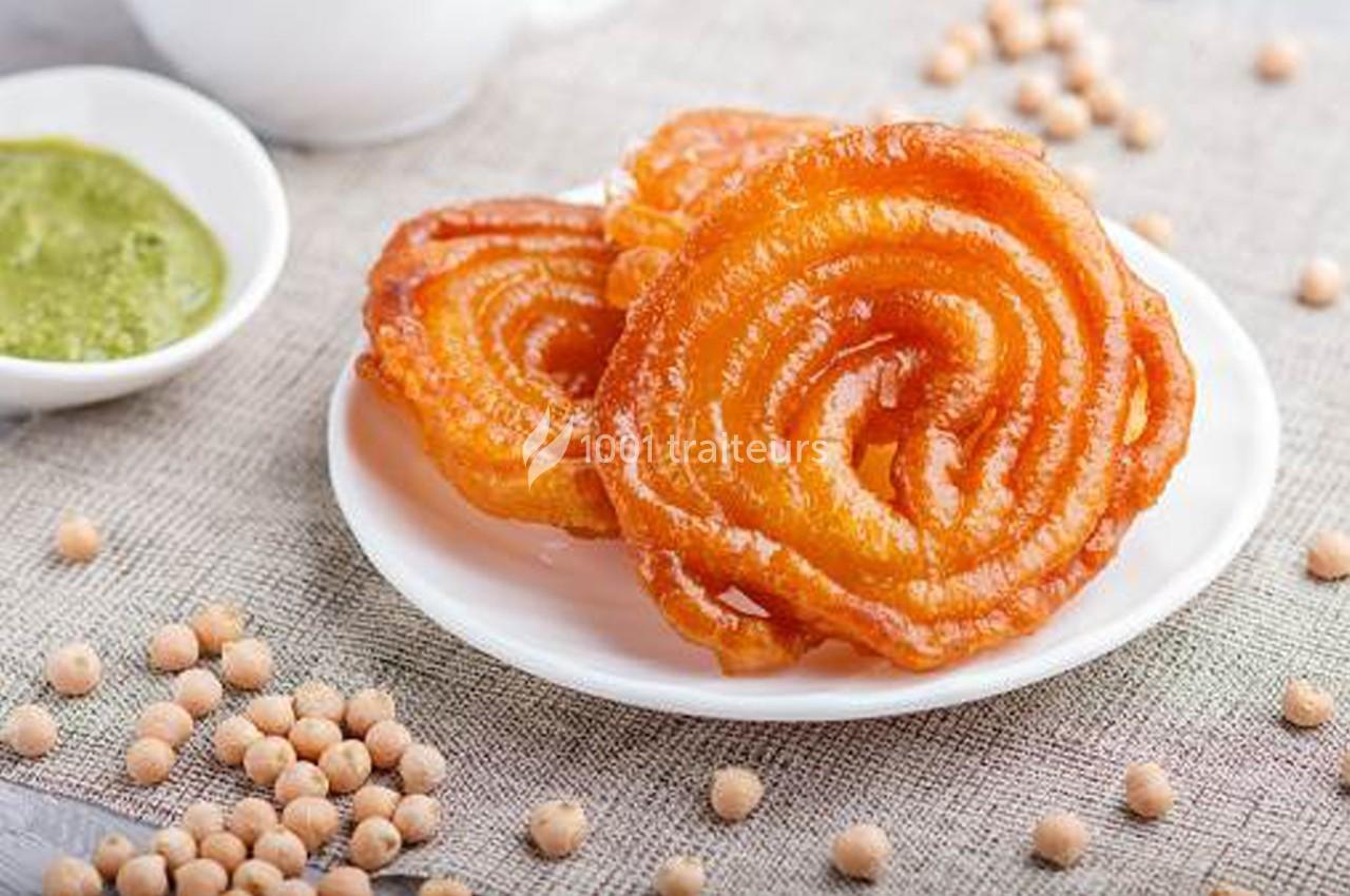 Assiette de jalebis dorés et croustillants, accompagnée d'une sauce verte et de pois chiches en arrière-plan.