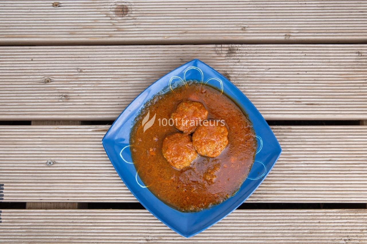 Assiette bleue contenant trois boulettes de viande dans une sauce rouge, posée sur une table en bois.