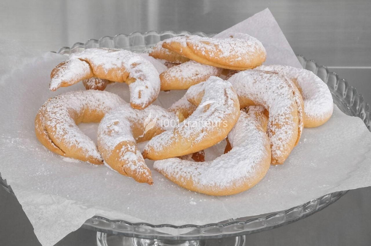 Assortiment de croissants sablés saupoudrés de sucre glace, disposés sur un plat en verre avec du papier cuisson.
