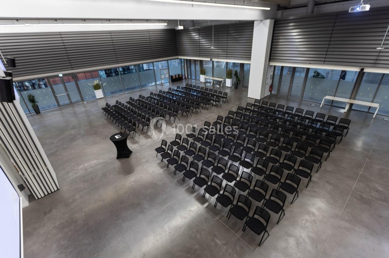 Salle moderne avec des rangées de chaises noires alignées, prête pour une conférence ou un événement.