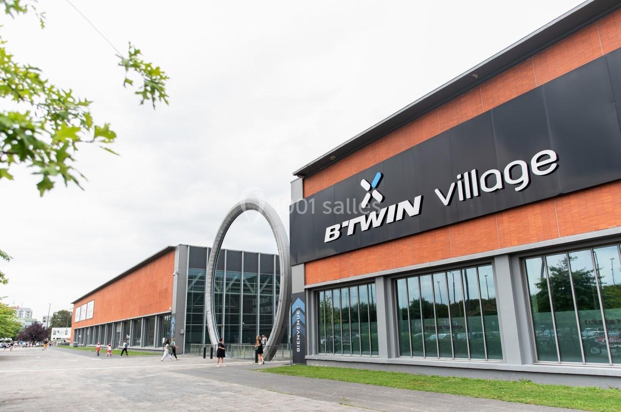 Façade du bâtiment B’Twin Village avec des murs en briques et une grande arche métallique à l’entrée.