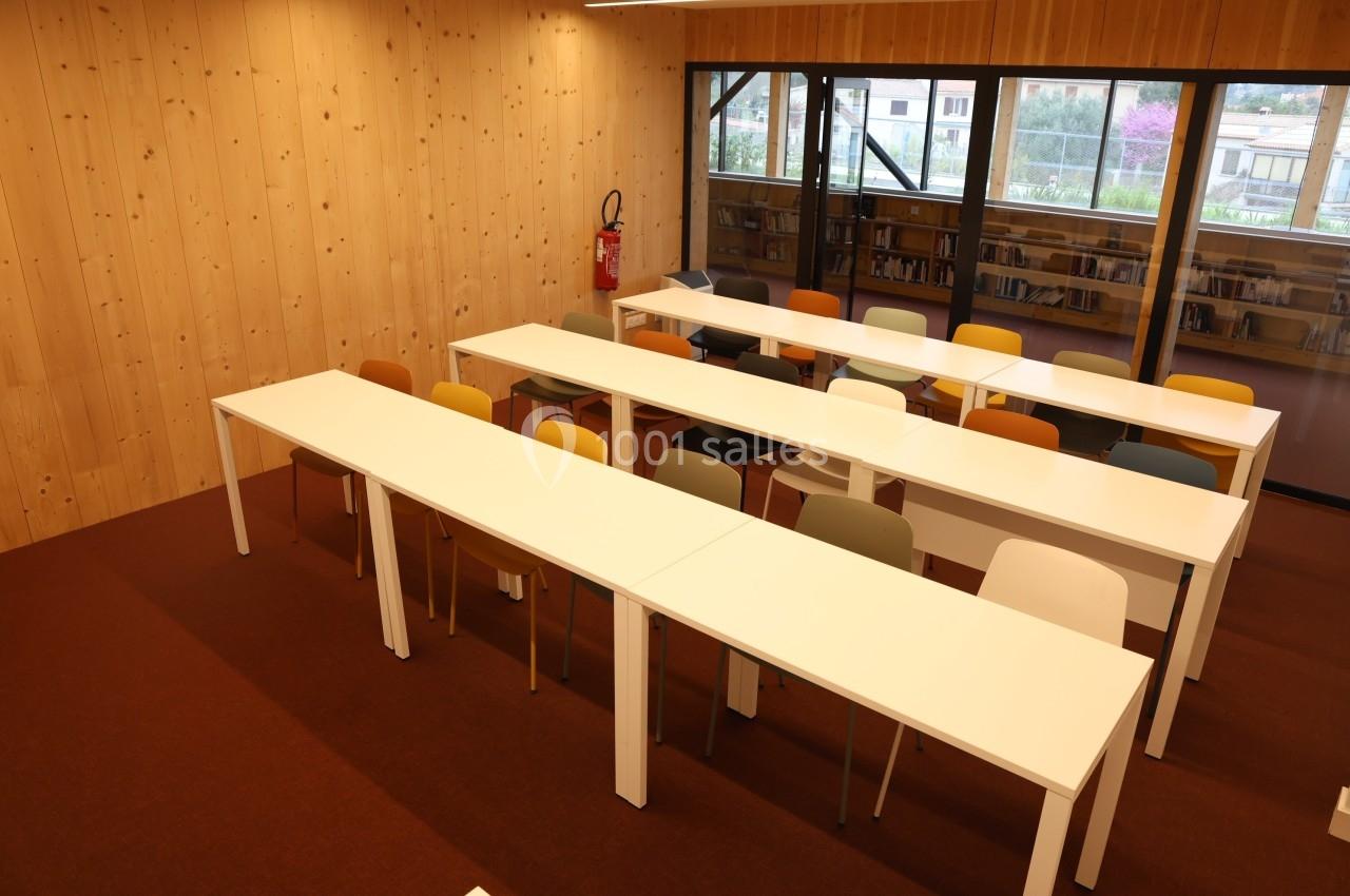 Salle de classe avec des tables blanches alignées, des chaises colorées et des murs en bois clair.