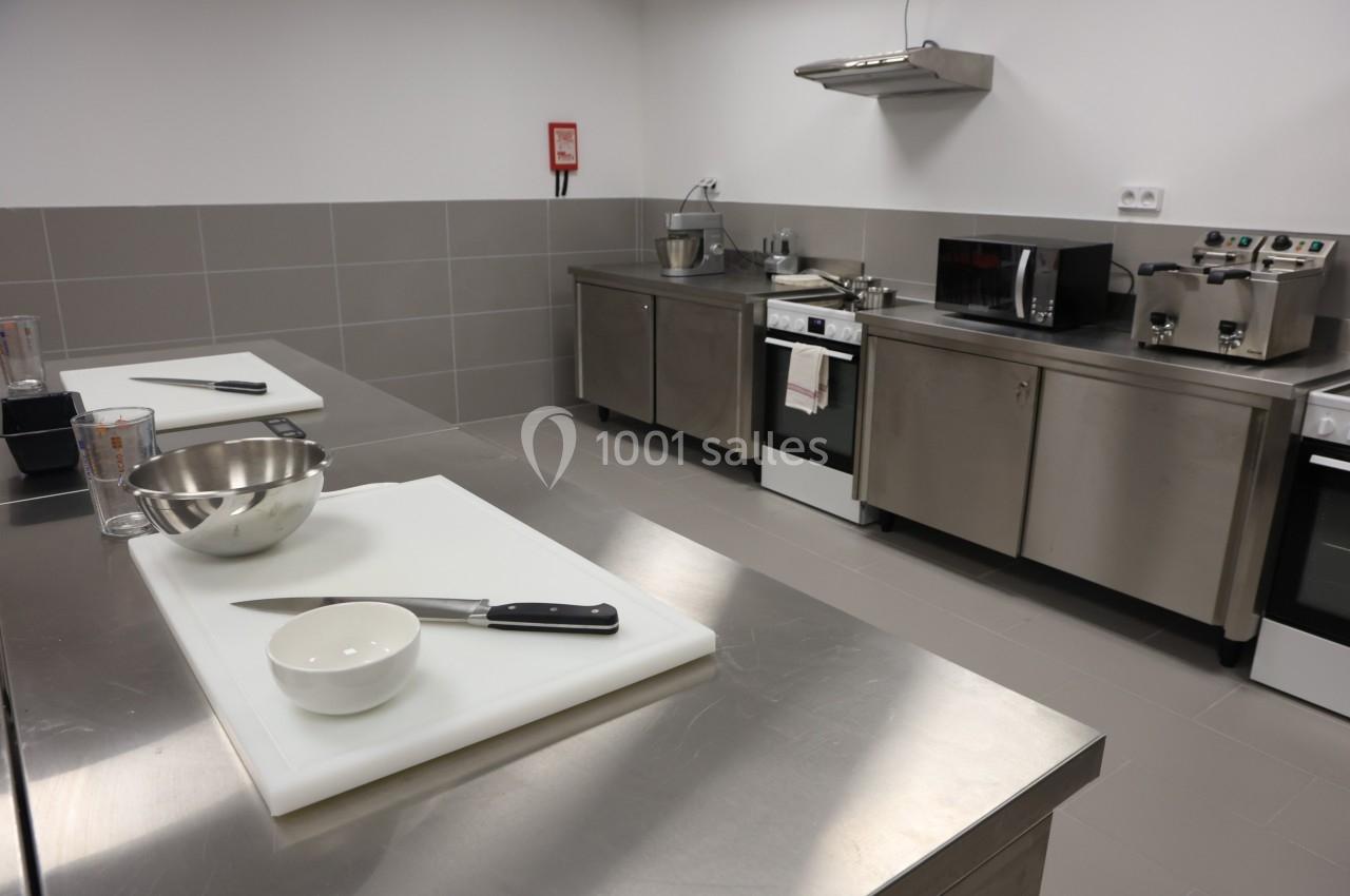 Plan de travail en cuisine professionnelle avec ustensiles, planches à découper et équipements en inox en arrière-plan.