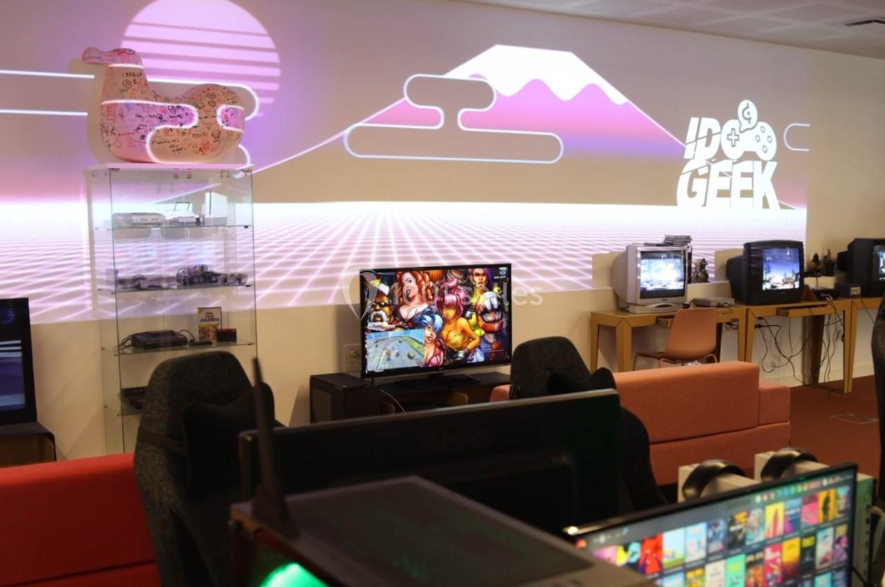 Salle aménagée avec des consoles de jeux rétro, des écrans allumés et une décoration murale néon rétro-futuriste.