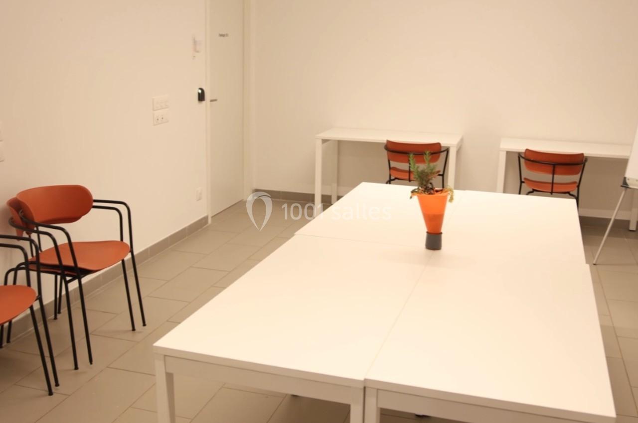 Salle de réunion lumineuse avec tables blanches, chaises orange et un tableau blanc sur pied.