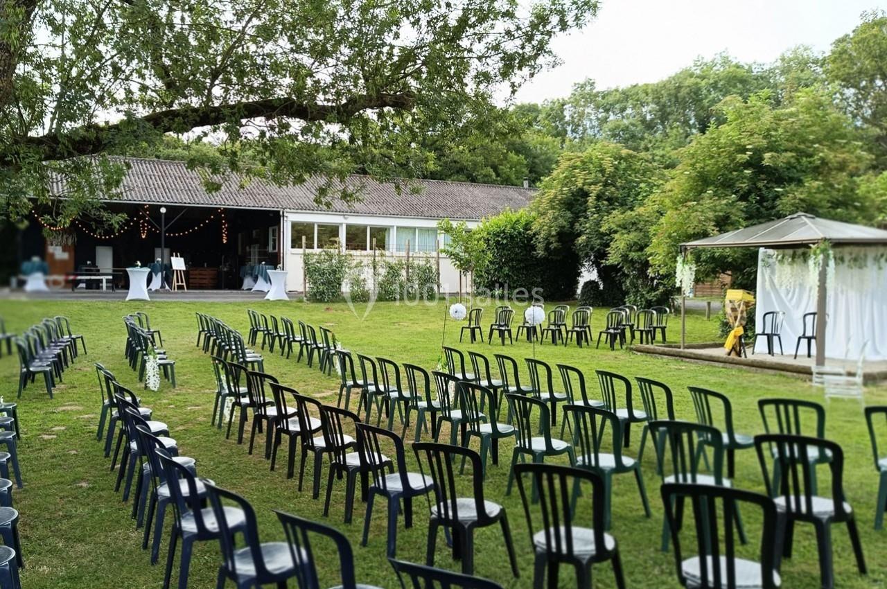 Chaises noires disposées en rangées sur une pelouse, face à une arche décorée pour une cérémonie en extérieur.