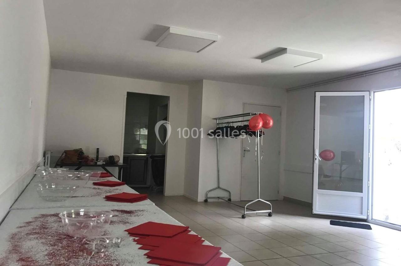 Salle lumineuse avec tables décorées de nappes blanches, paillettes rouges, serviettes pliées et porte ouverte sur l…