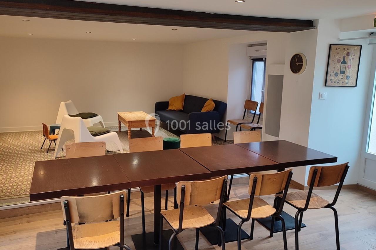 Salle lumineuse avec table en bois, chaises, canapé bleu, fauteuils blancs et décoration murale minimaliste.