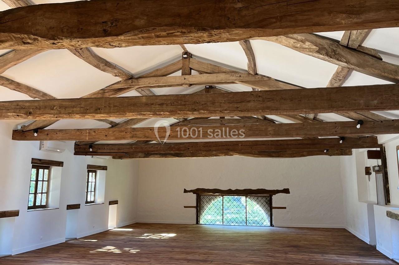 Salle lumineuse avec poutres apparentes en bois, parquet au sol et fenêtres laissant entrer la lumière naturelle.