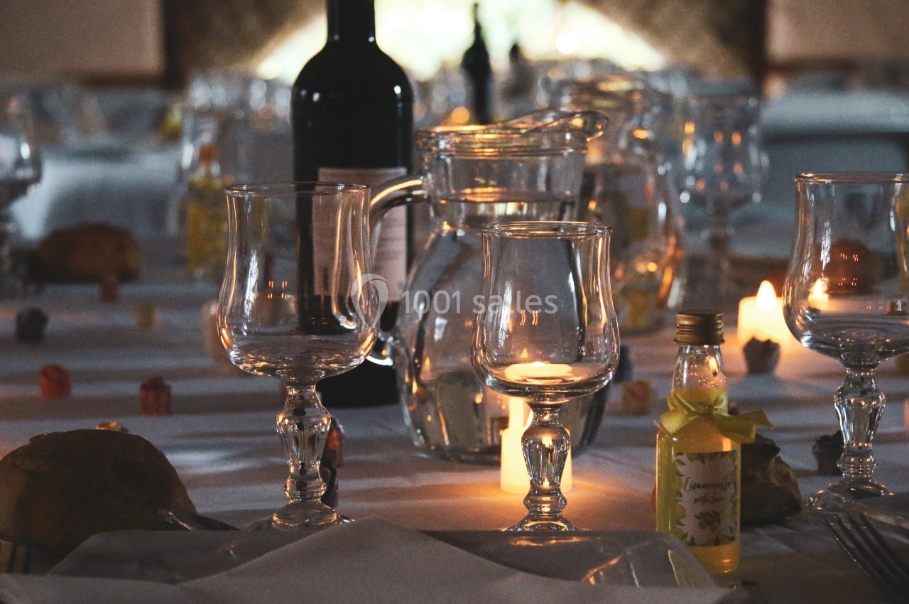 Table dressée avec des verres, une carafe, une bouteille de vin et des bougies allumées dans une ambiance tamisée.