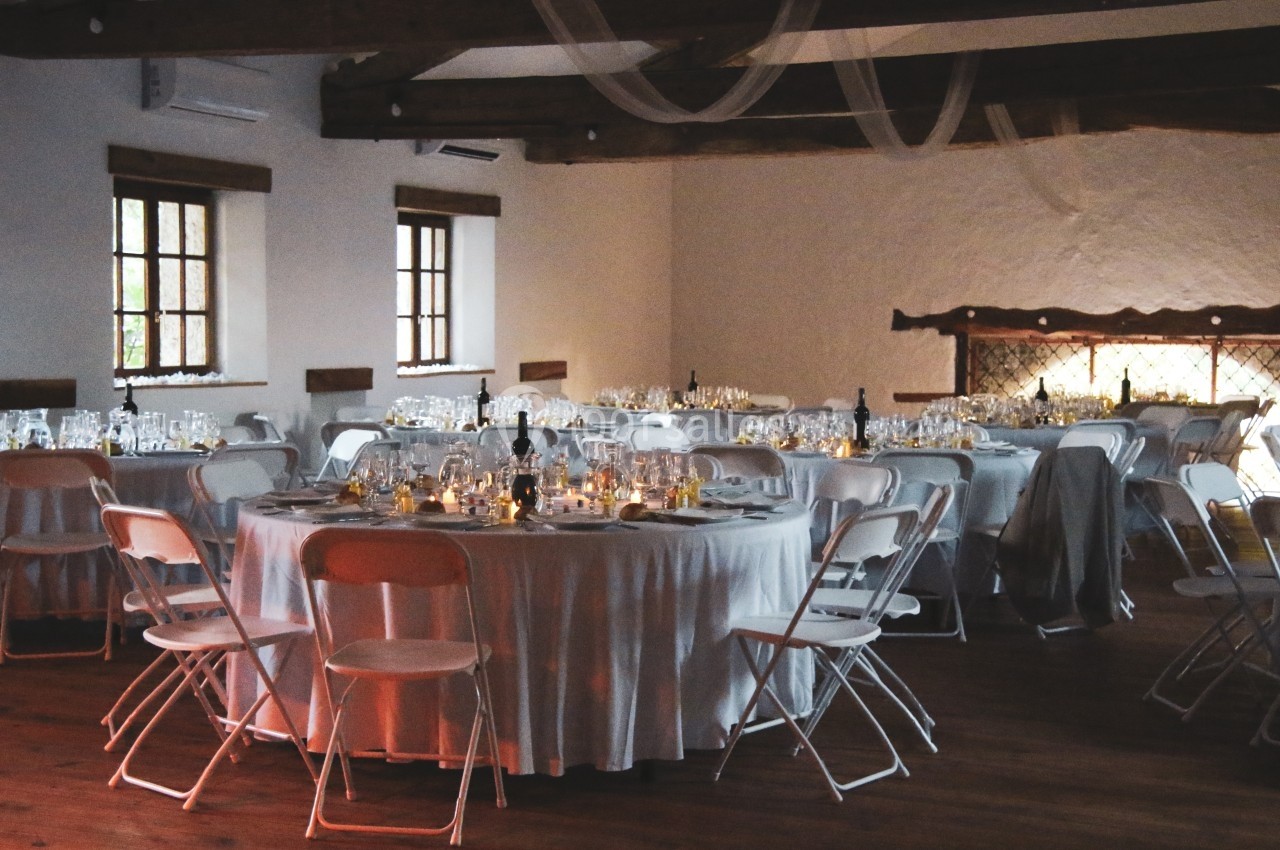 Salle de réception décorée avec des tables rondes, nappes blanches, chaises pliantes et lumière tamisée.