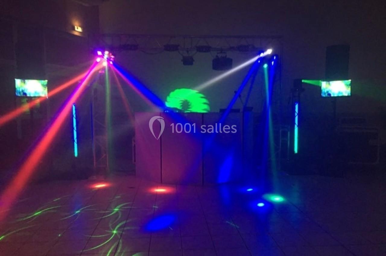 Jeu de lumières colorées projetées dans une salle sombre avec des écrans et un équipement de sonorisation.