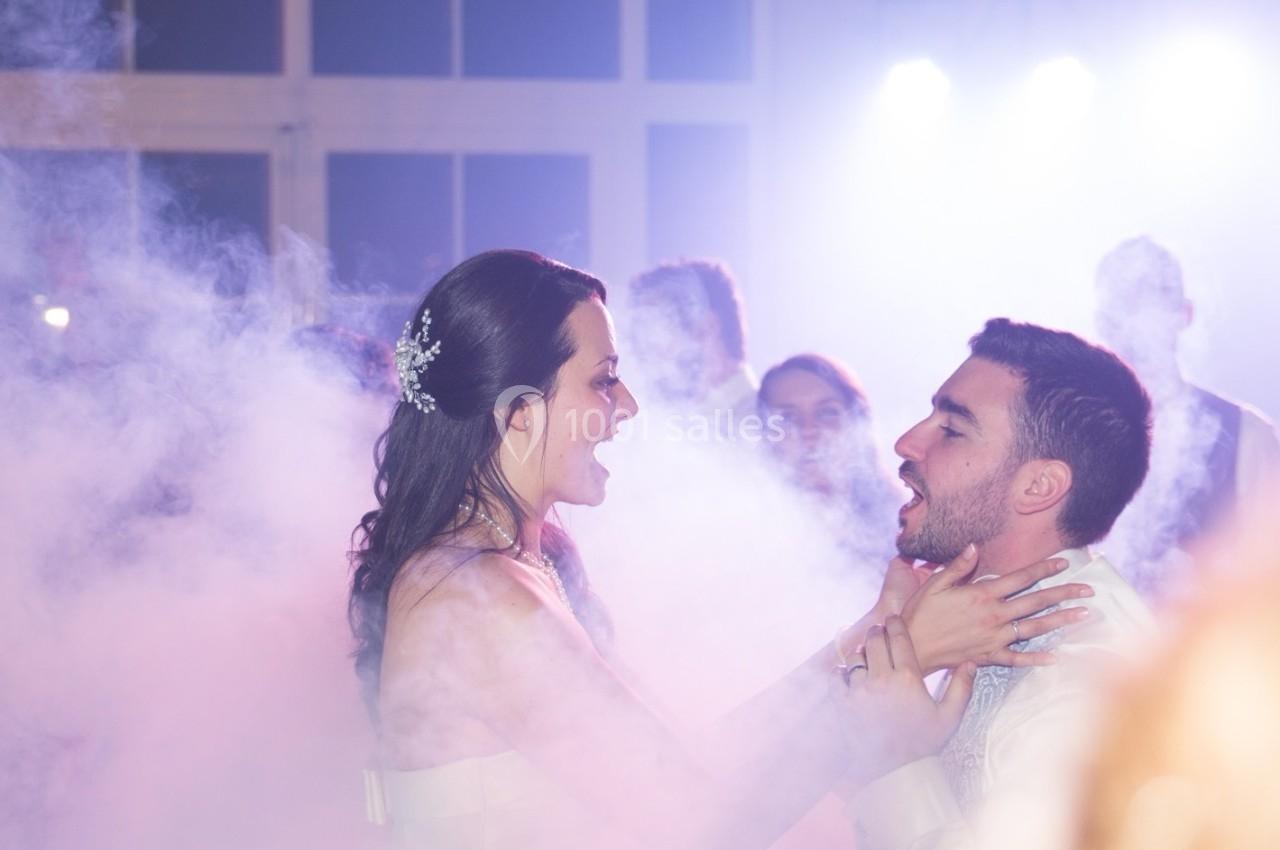Une femme et un homme dansent au milieu de la fumée, entourés d'autres personnes dans une ambiance festive.