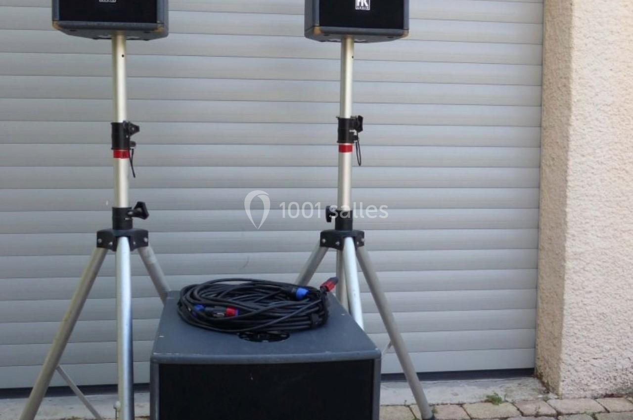 Deux enceintes sur trépieds et un caisson de basses posés sur un sol pavé devant une porte de garage.