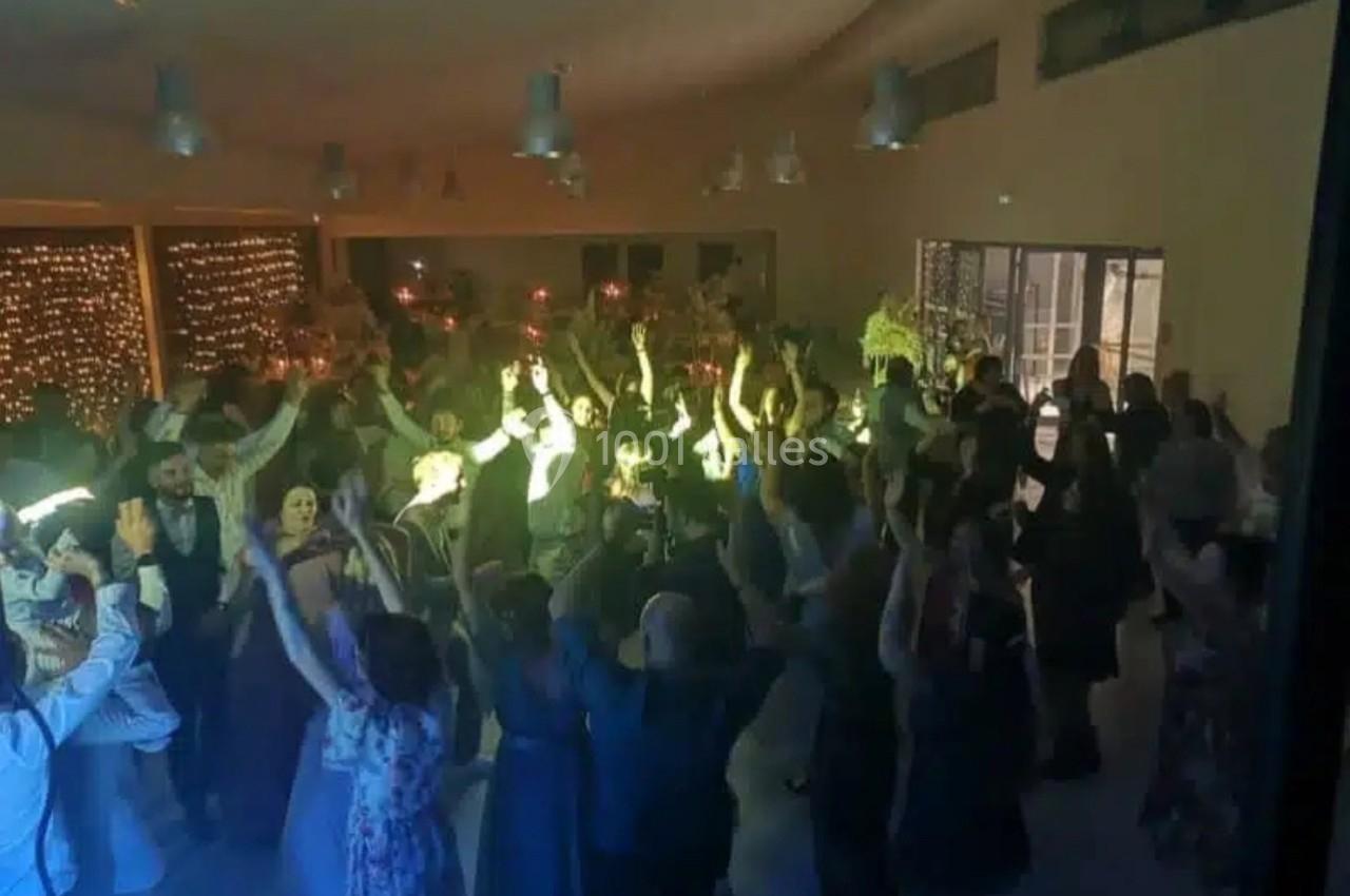 Groupe de personnes dansant dans une salle éclairée, décorée de guirlandes lumineuses et de tables festives.
