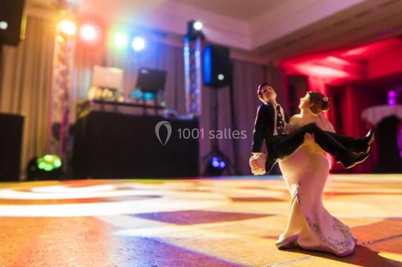 Figurines de mariés dansant sur une piste éclairée, avec une scène et des lumières colorées en arrière-plan.