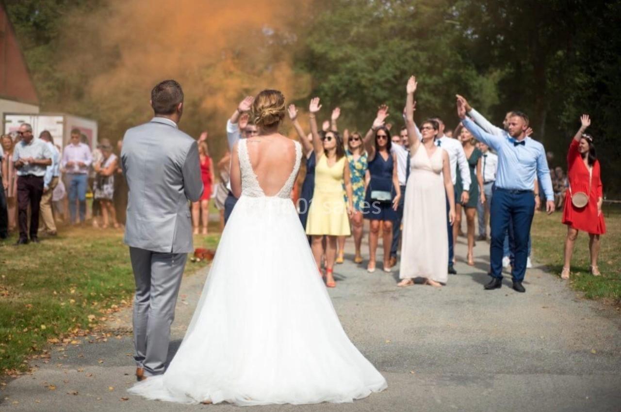 Un couple de mariés fait face à un groupe d'invités levant les bras lors d'une célébration en extérieur.
