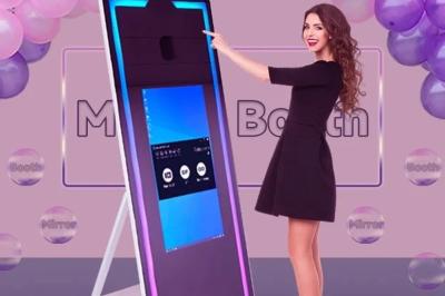 Deux femmes souriantes se tiennent près d'une borne photo dans un espace intérieur avec des tables et des chaises en arrière…