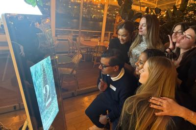 Deux femmes souriantes se tiennent près d'une borne photo dans un espace intérieur avec des tables et des chaises en arrière…