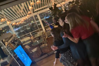 Deux femmes souriantes se tiennent près d'une borne photo dans un espace intérieur avec des tables et des chaises en arrière…