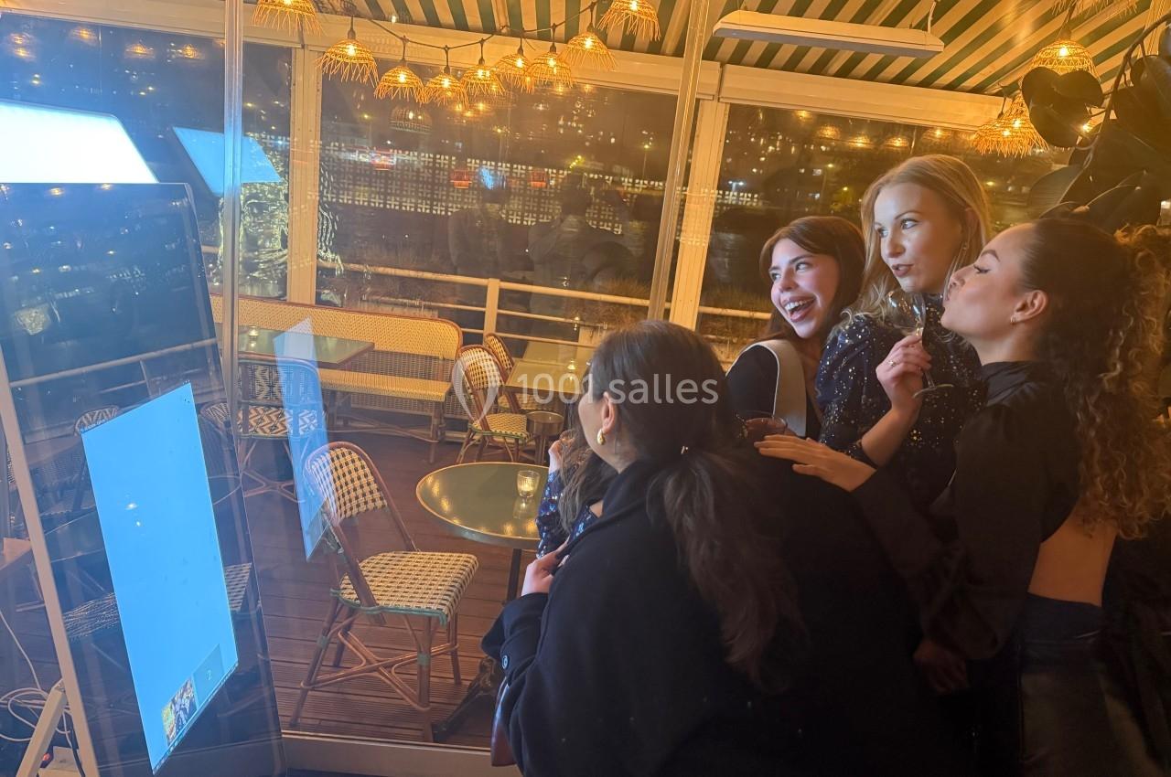 Quatre femmes souriantes utilisent une borne photo interactive dans un espace lumineux et décoré de guirlandes.