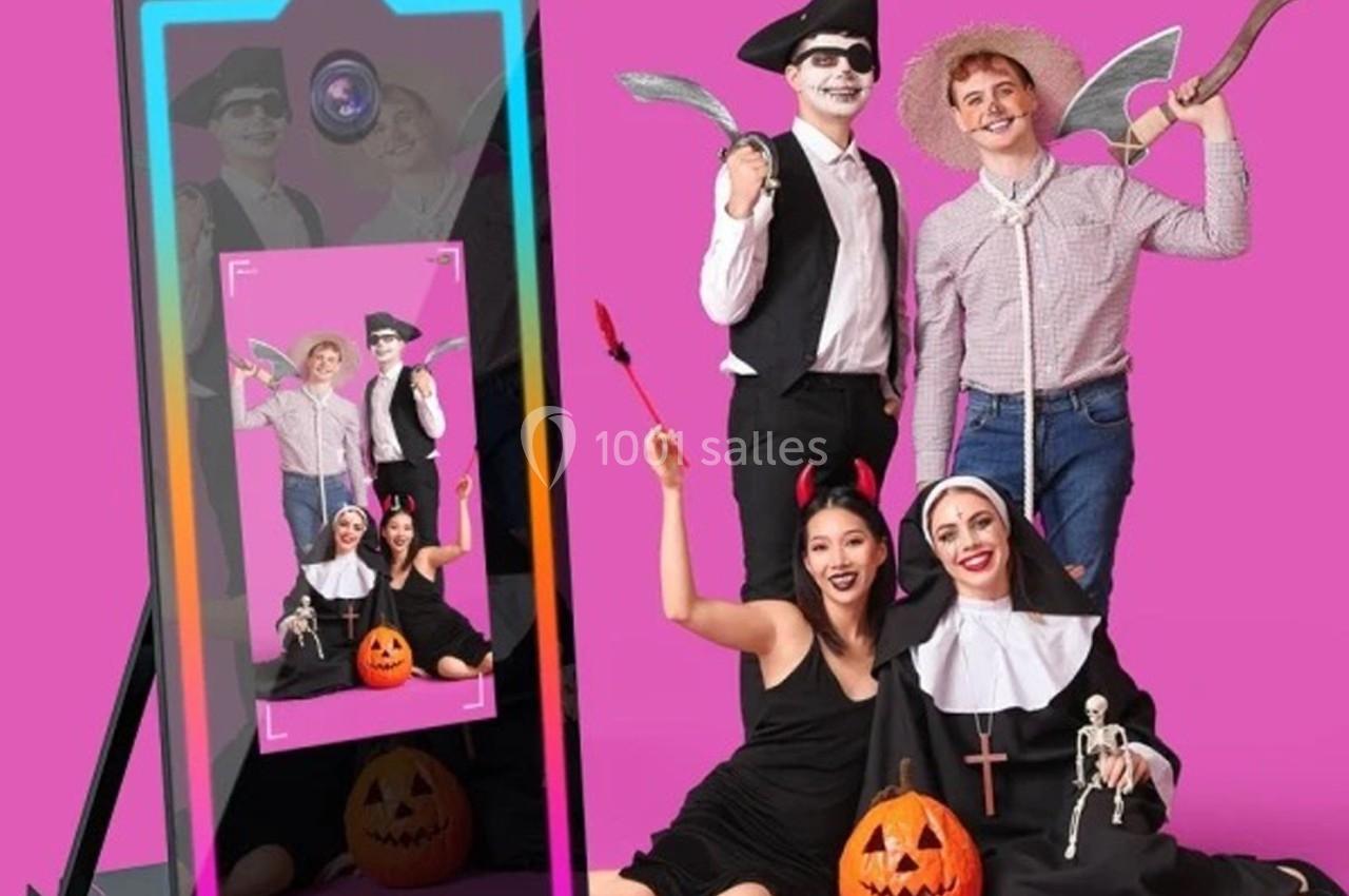 Deux personnes déguisées posent devant un smartphone affichant leur photo, accompagnées de deux autres en arrière-plan.