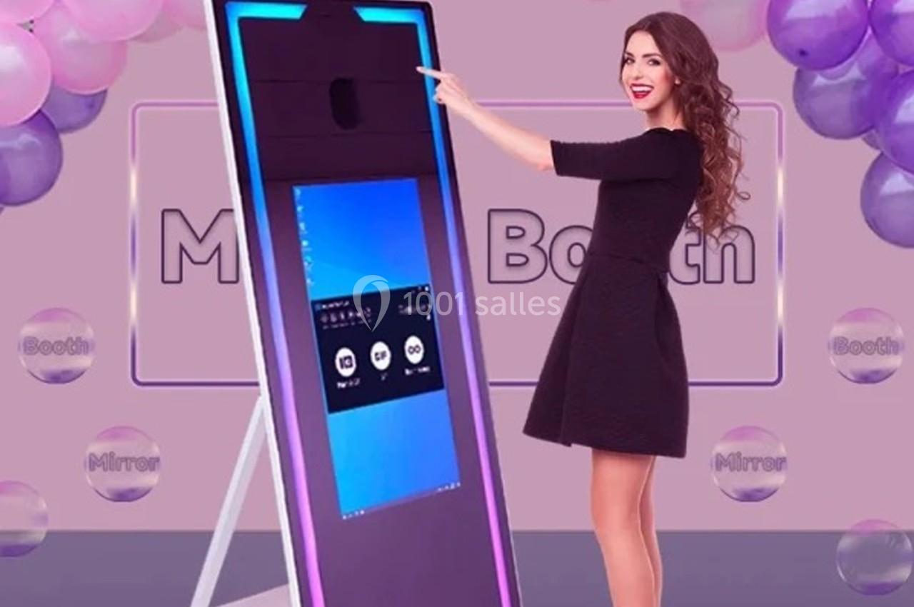 Femme interagissant avec un miroir photo interactif entouré de ballons dans un décor festif.