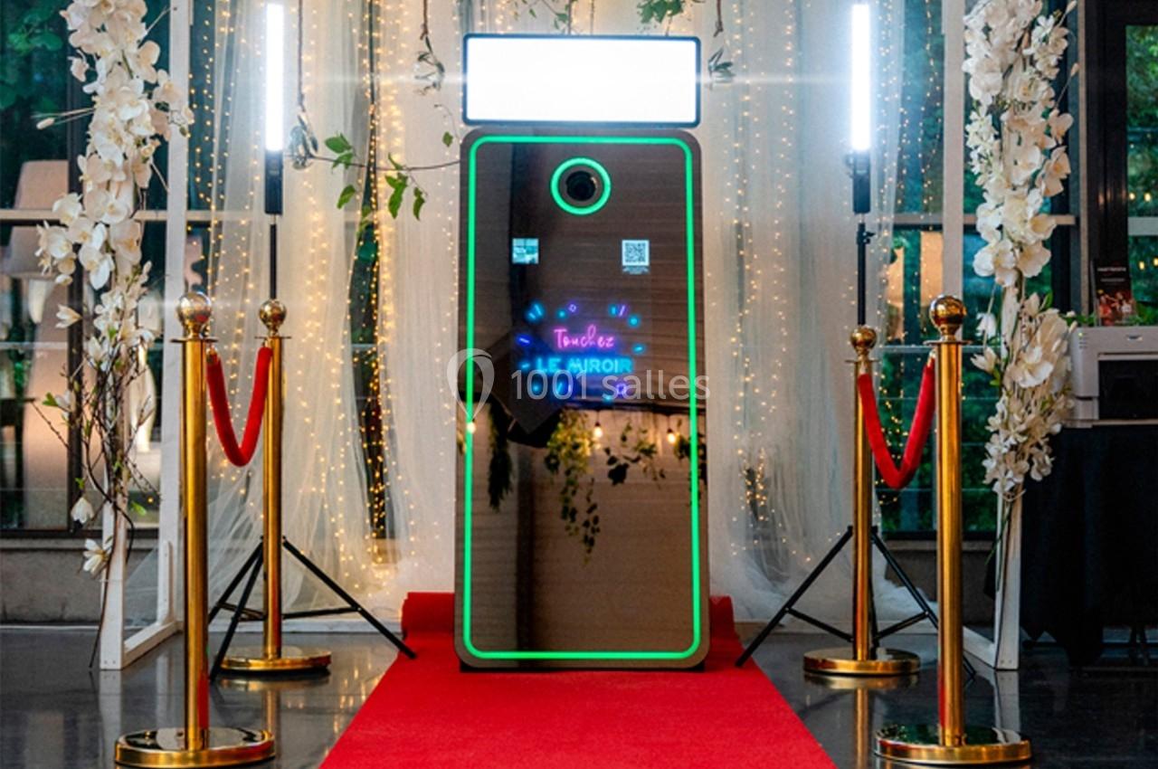 Miroir interactif lumineux entouré de décorations festives, avec tapis rouge et cordons dorés.