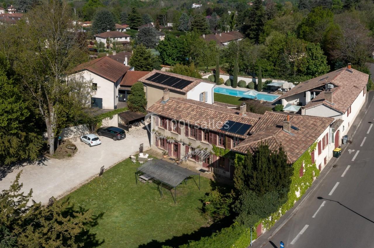 Vue aérienne d'une propriété avec plusieurs bâtiments, panneaux solaires sur les toits, piscine et végétation environnante.