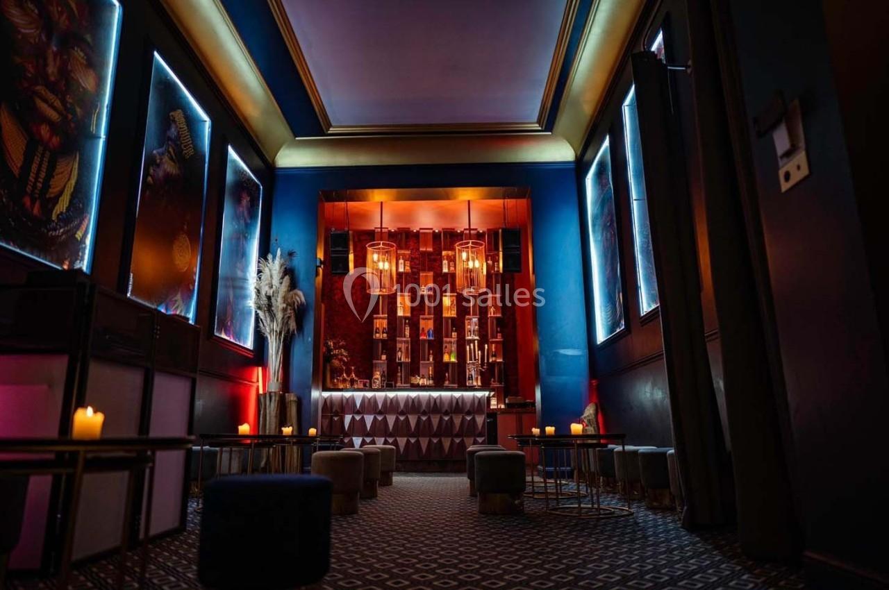 Salle de bar élégante avec éclairage tamisé, murs bleus, décorations modernes et bougies sur des tables basses.