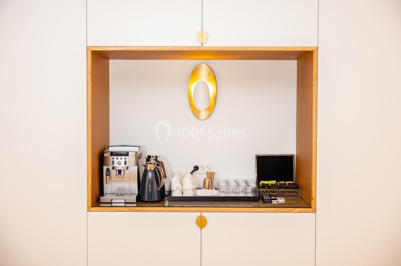 Espace kitchenette avec machine à café, bouilloire, tasses, verres et accessoires disposés sur une étagère encastrée.