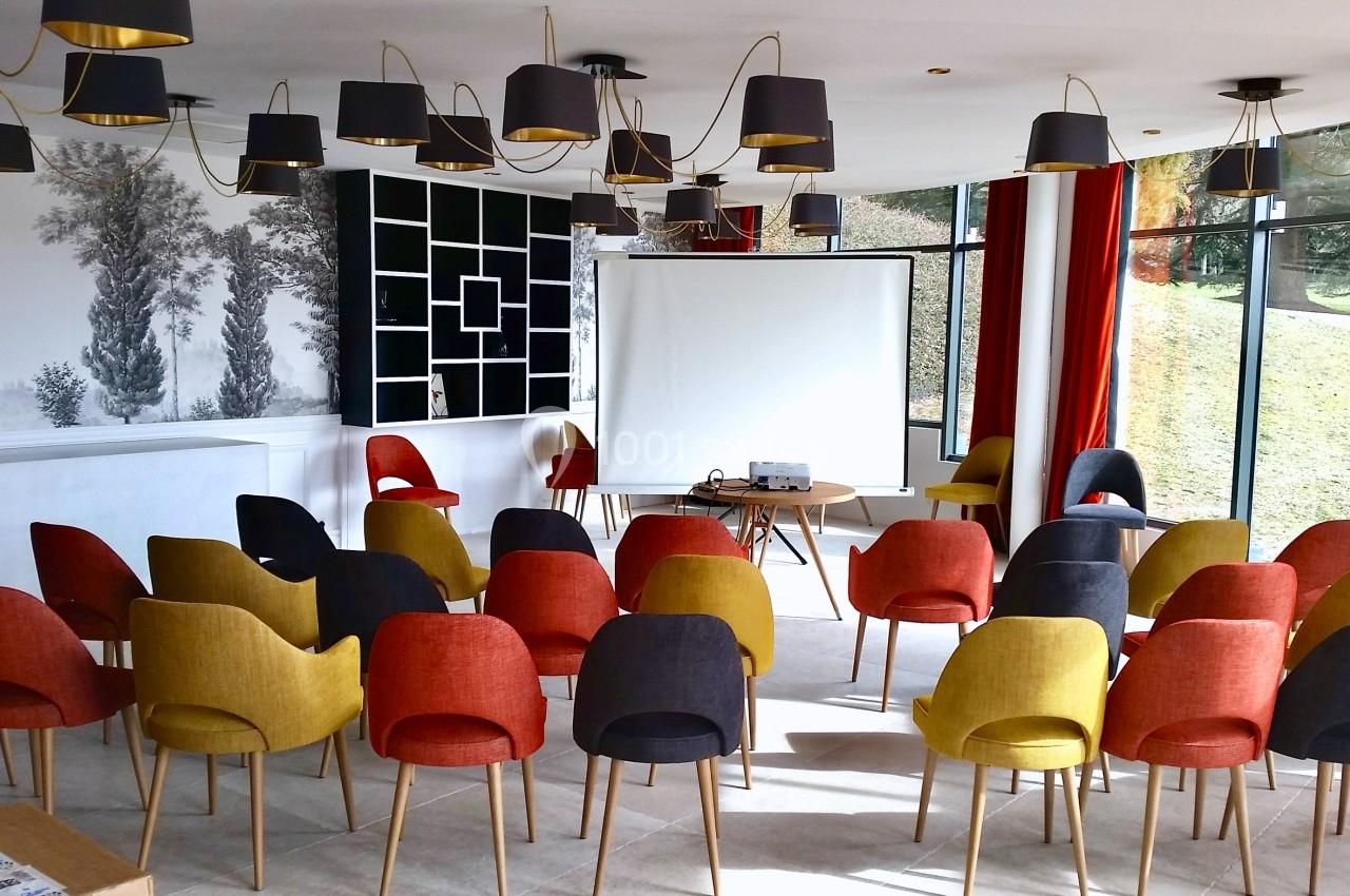 Salle lumineuse aménagée avec des chaises colorées disposées face à un écran de projection.