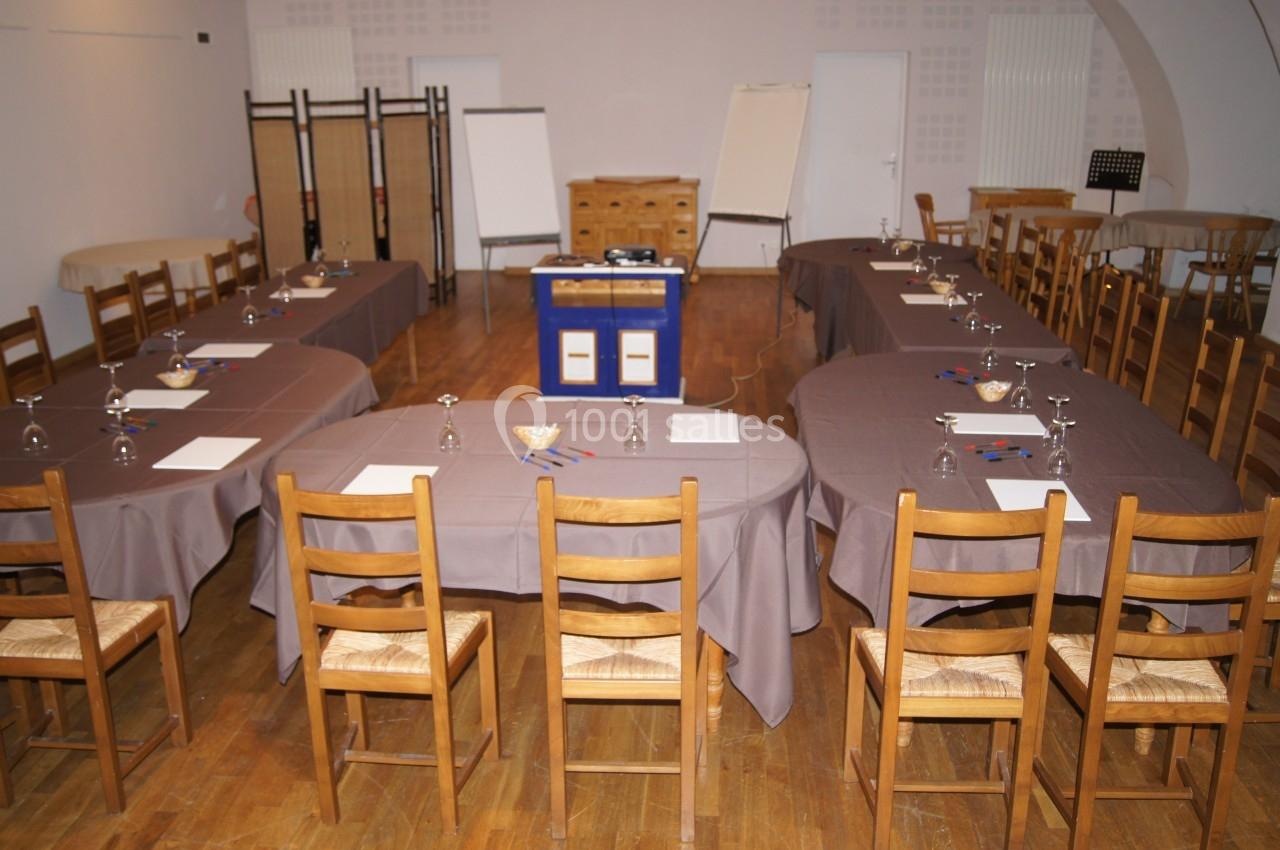 Salle de réunion aménagée en U avec tables, chaises en bois, verres, blocs-notes et matériel de présentation.