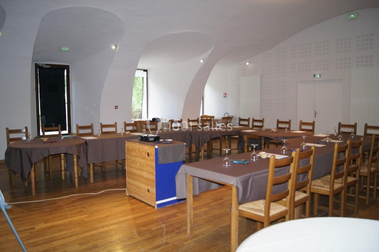 Salle de réunion lumineuse avec tables disposées en U, chaises en bois et équipement de présentation sur un meuble.