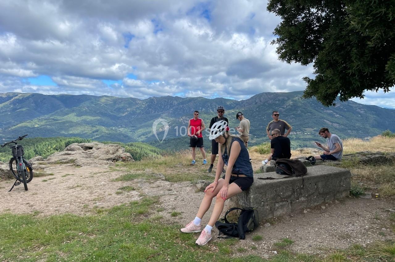 Un groupe de personnes se repose en plein air sur une colline avec vue sur des montagnes et un ciel partiellement nuageux.