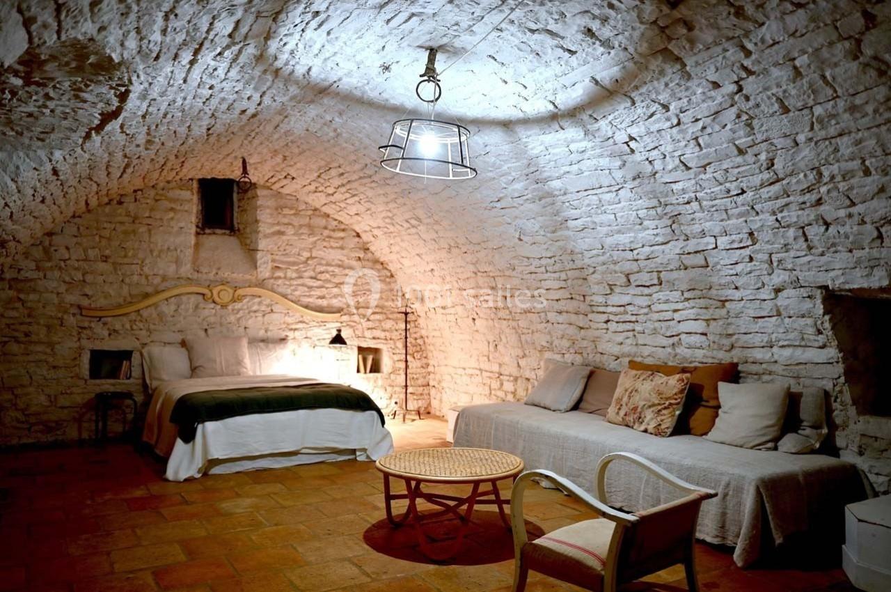 Chambre voûtée en pierre avec lit double, canapé, table basse en rotin et éclairage suspendu.