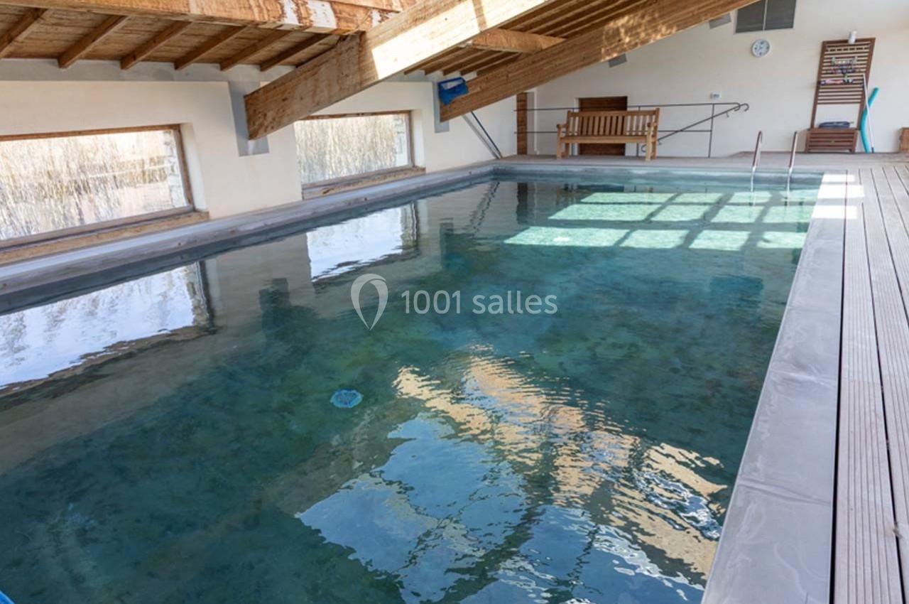 Piscine intérieure avec toit en bois, entourée de grandes fenêtres laissant entrer la lumière naturelle.