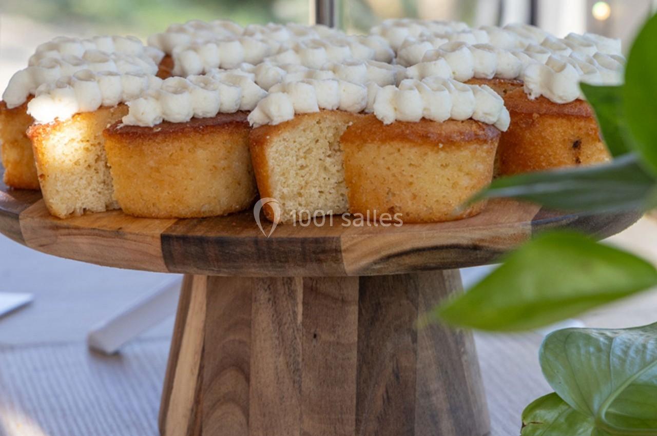 Des petits gâteaux dorés avec glaçage blanc sont disposés sur un présentoir en bois, éclairés par la lumière naturelle.