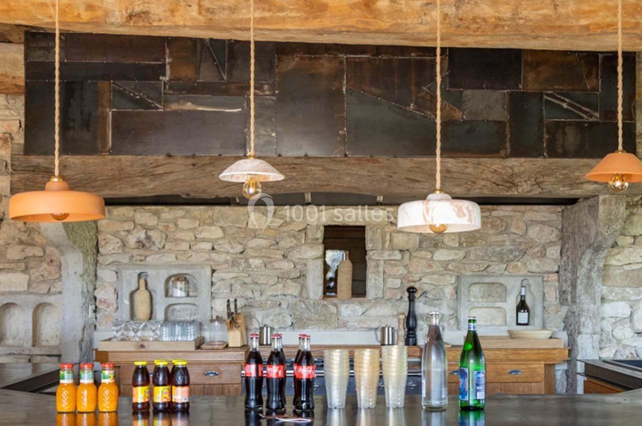 Comptoir de cuisine rustique avec boissons variées, lampes suspendues et mur en pierre apparente.