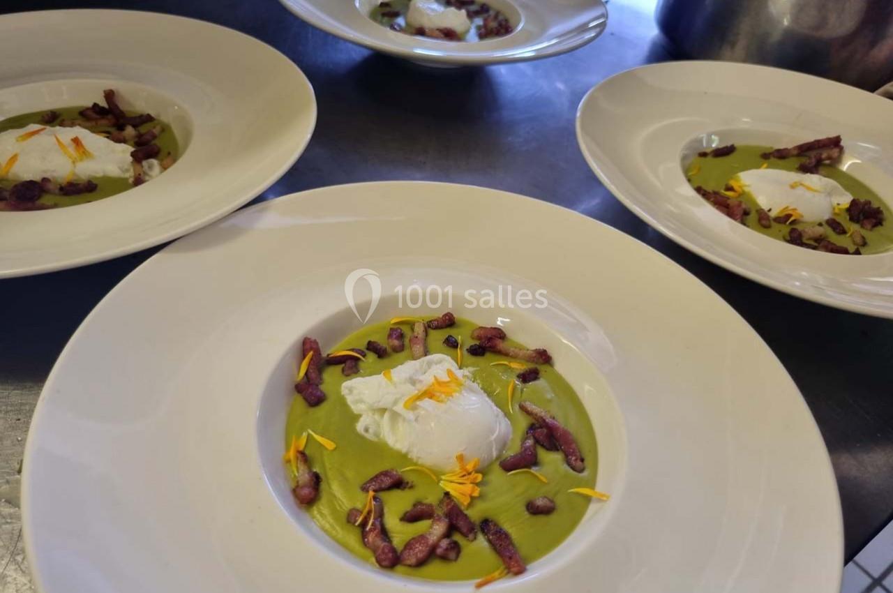 Assiette contenant une soupe verte garnie d'un œuf poché, de croûtons violets et de pétales de fleurs comestibles.