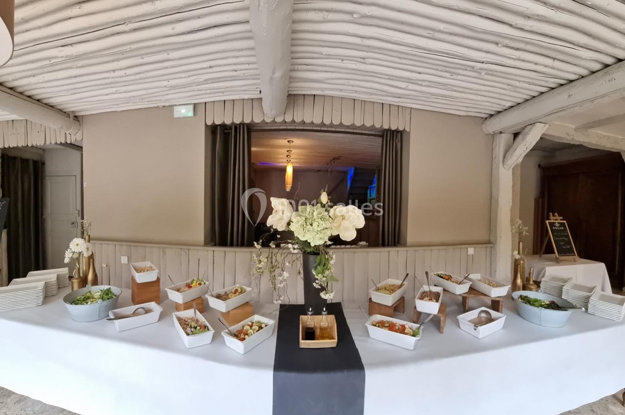 Buffet composé de salades variées, fleurs blanches en centre de table, dans une salle au plafond en bois peint.