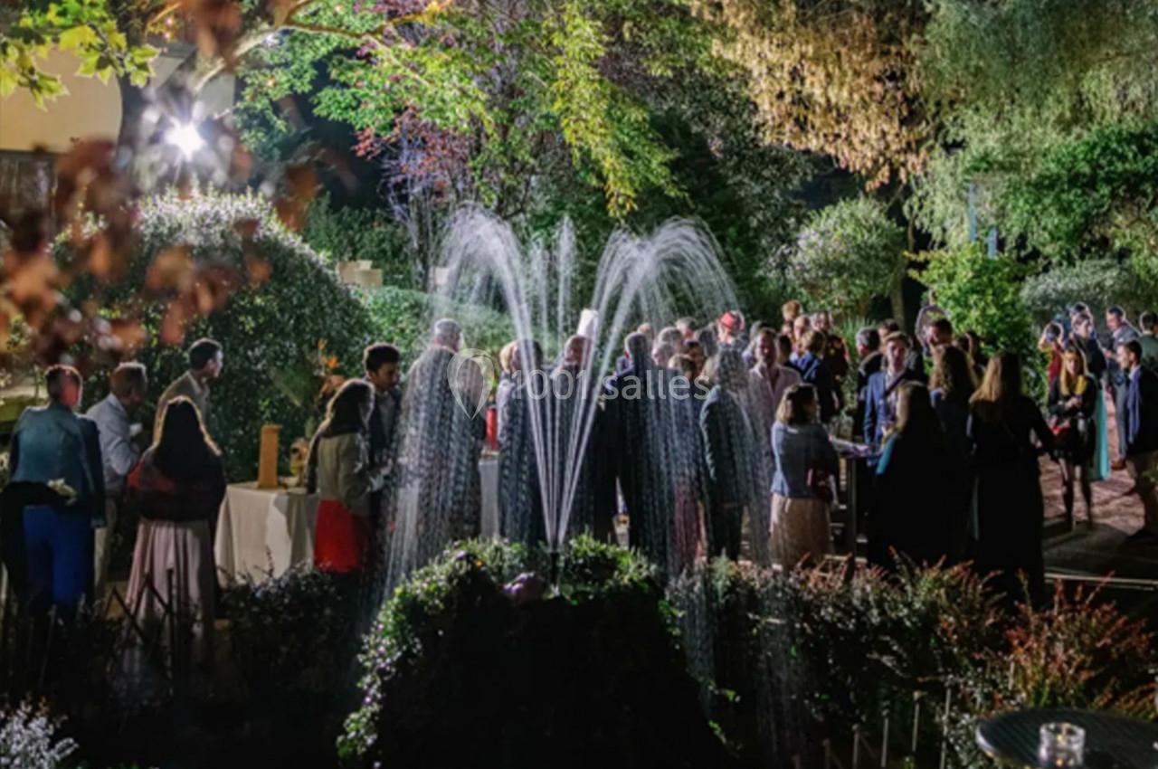 Groupe de personnes rassemblées dans un jardin éclairé la nuit, près d'une fontaine en fonctionnement.