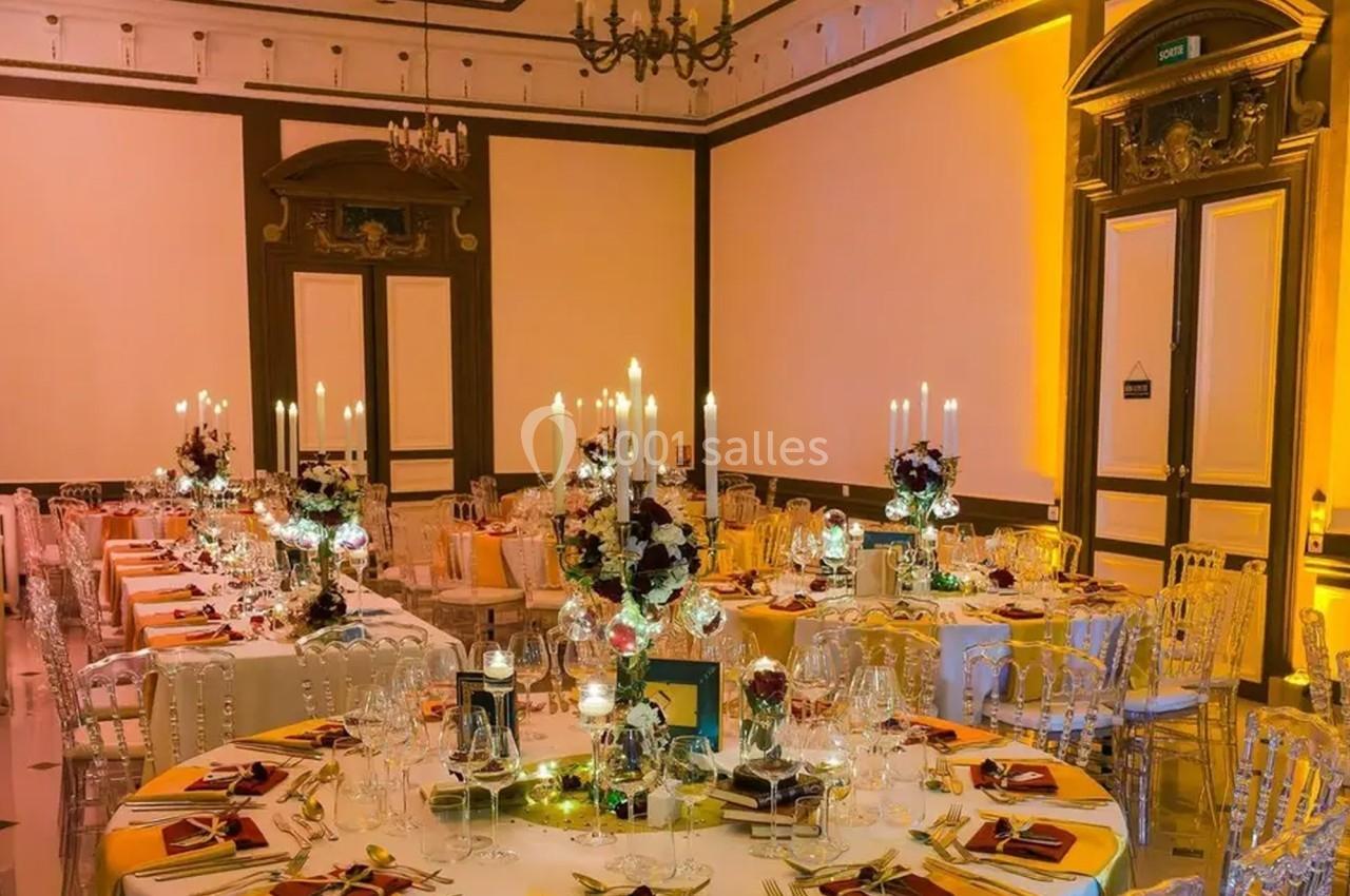 Salle de réception élégamment décorée avec des tables rondes, des chandeliers et des compositions florales.
