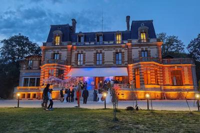 Centre de table floral avec roses roses, fleurs violettes et blanches, entouré de bougies et de verres sur une nappe blanche.