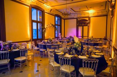 Centre de table floral avec roses roses, fleurs violettes et blanches, entouré de bougies et de verres sur une nappe blanche.
