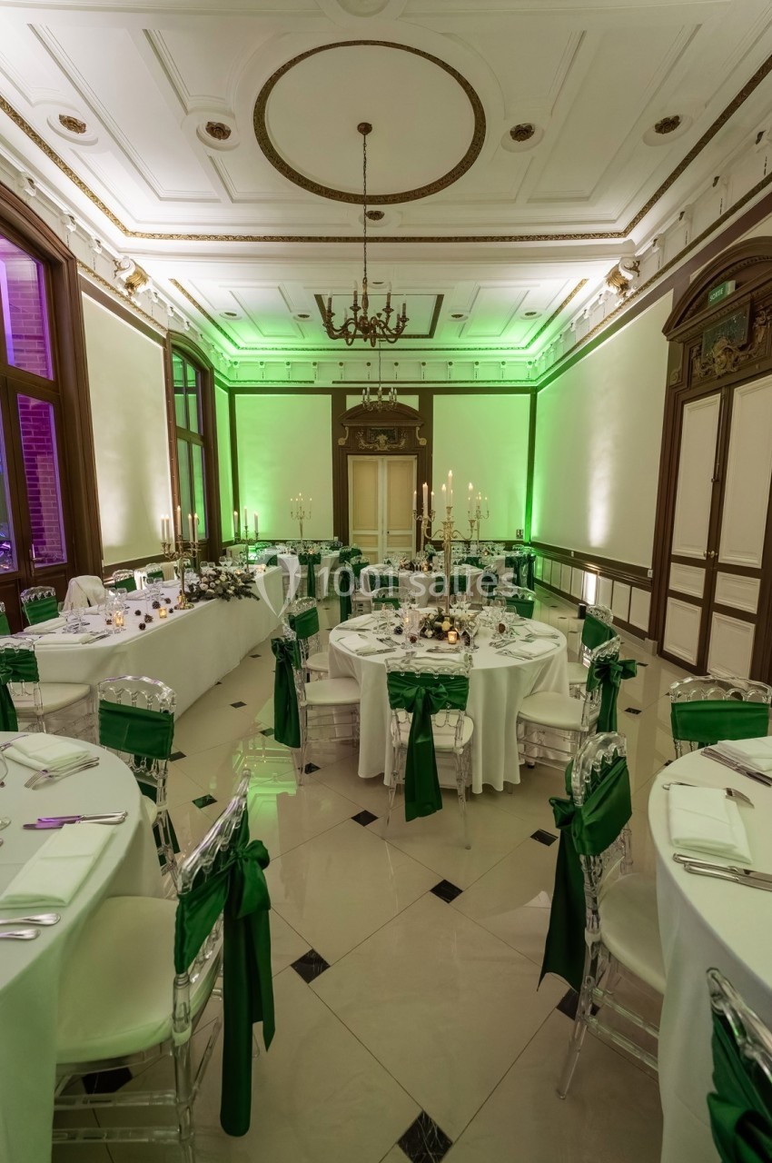 Salle de réception élégante avec tables rondes décorées de nappes blanches et de chaises ornées de rubans verts.