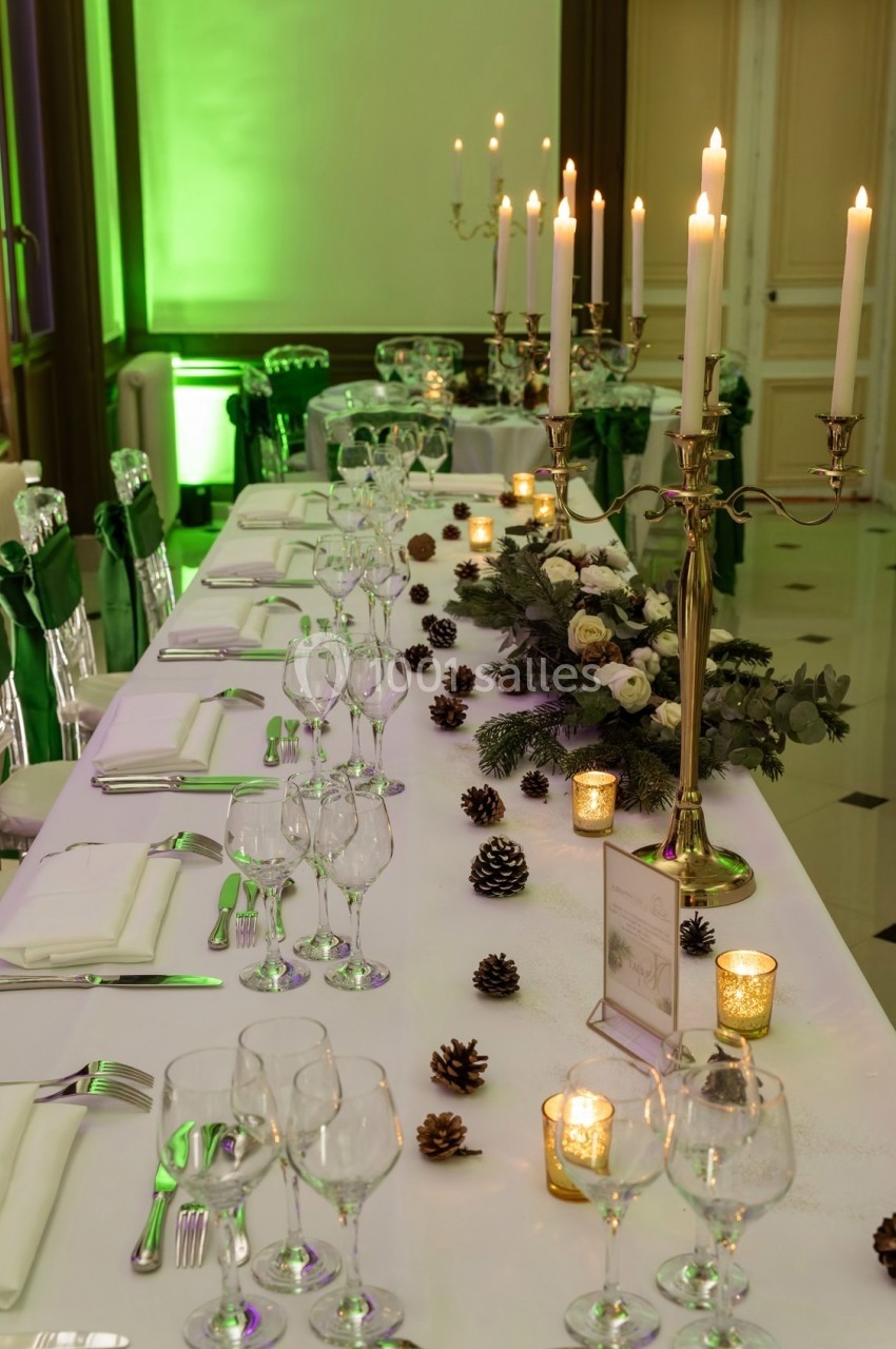 Table de réception élégamment décorée avec chandeliers, bougies, pommes de pin et fleurs blanches.